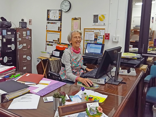 Betty sitting behind a desk working at a computer while smiling at the camera