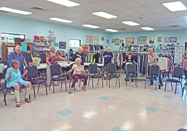 group of seniors standing or sitting in chairs in a line doing exercises together - Casa Events